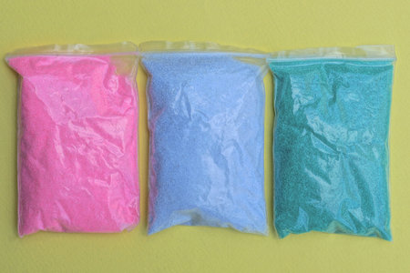 three small plastic bags full of colored sand lie on a yellow tableの写真素材