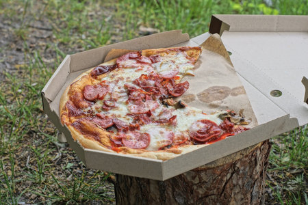 food and one round colored pizza carbonara in a gray paper carton box in the street in natureの写真素材