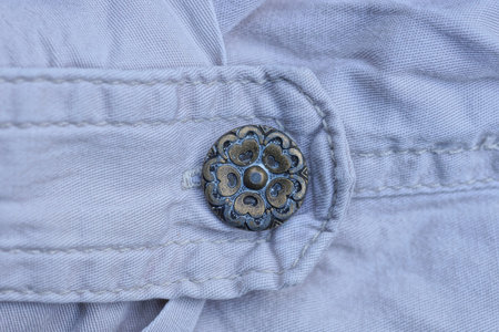 one brown black metal button on a harness on a pocket made of white fabric on clothes