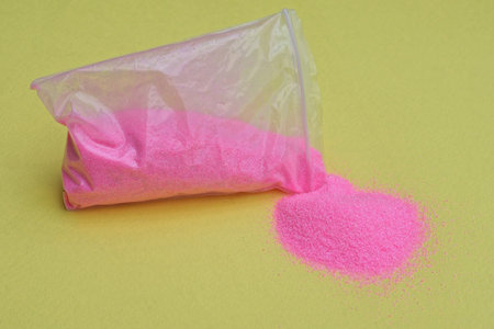 one small plastic bag with pink spilled sand on a yellow table