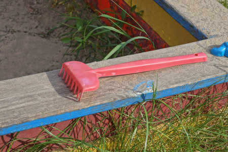 one small red plastic toy rake lies on a wooden sandbox board outside in the playgroundの写真素材