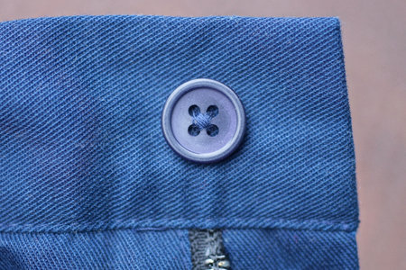 one blue plastic button on the fabric of the jacket sleeve on a brown backgroundの写真素材