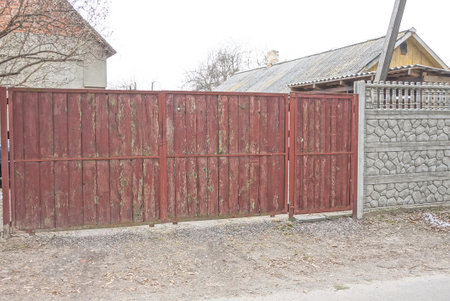 long red wooden gate and closed door near gray concrete fence wall on rural street