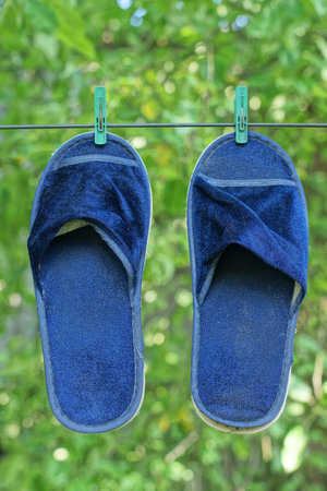 two blue summer slippers hang on a wire in the street among green vegetationの写真素材