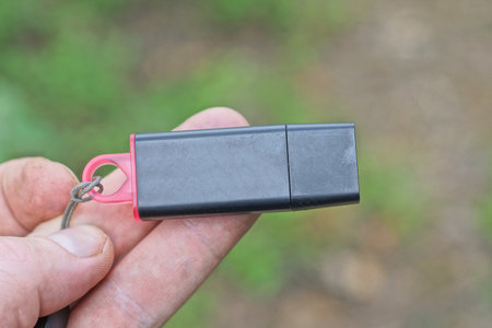 fingers on the hand hold one black small plastic compact flash drive outdoors on a gray green backgroundの写真素材