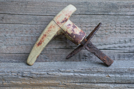 detail from one small old door handle made of gray plastic and brown rusty iron lies on a wooden tableの写真素材