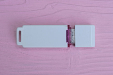 one small white plastic closed mobile flash drive lies on a pink wooden table