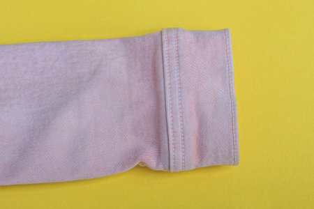 one pink sleeve of a jacket made of satin fabric lies on a yellow table