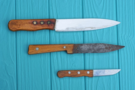 a row of three old knives with brown handles lie on a blue wooden table