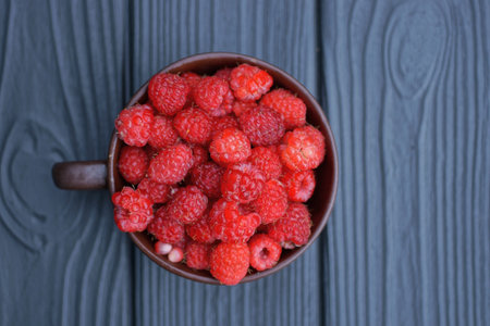 red ripe raspberries in a brown cup on a black wooden table