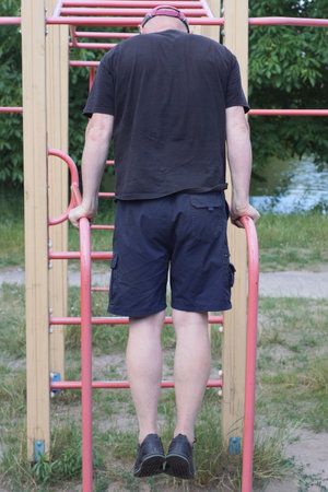 one male athlete in a black shirt trains on red metal sports bars on a sports ground on the street