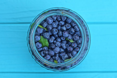 ripe fresh blueberries in a glass jar on a blue table