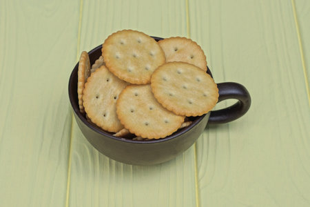 a pile of brown round cookies in a cup stands on a yellow wooden table