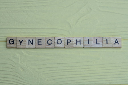 the word gynecophilia of gray small wooden letters lies on a yellow wooden tableの写真素材