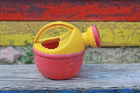 one small colored plastic watering can toy stands on a gray wooden table outsideの写真素材