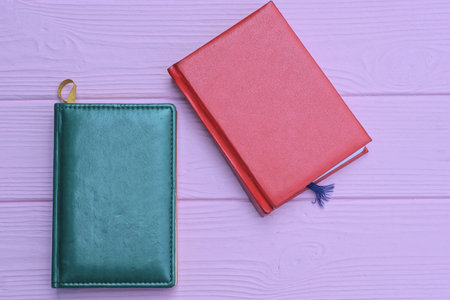 closed red and green leather notebooks lie on a pink tableの写真素材
