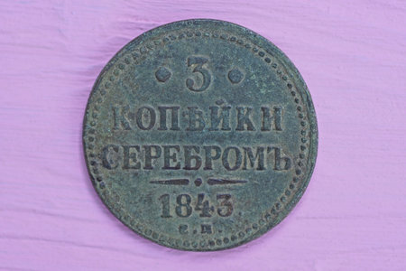 one big old gray copper coin lies on a pink wooden table
