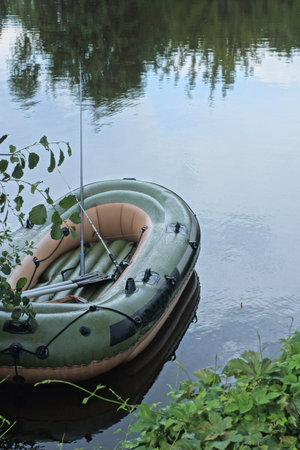 one empty rubber boat with a fishing rod and oars on the water of a lake near the shore in green vegetationの写真素材
