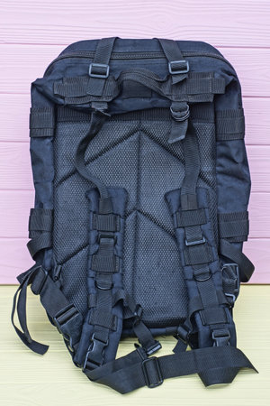 one large army black backpack stands on a yellow wooden table against a pink wall