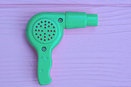 one small green plastic toy electric hair dryer lies on a pink wooden tableの写真素材