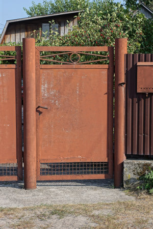 one closed brown red metal door on a fence wall in a rural streetの写真素材