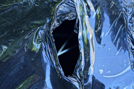a piece of old black torn cellophane with a hole in the packaging