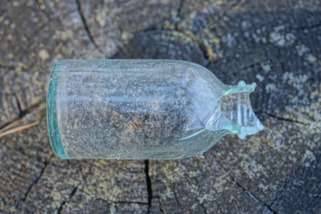 one small dirty white glass old bottle with a broken neck lies on a gray wooden table