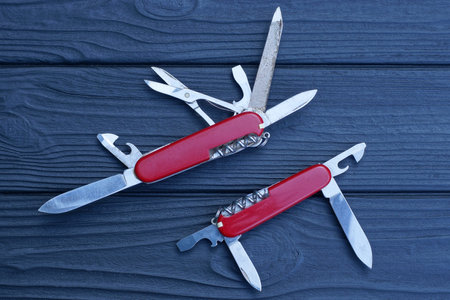 two open folding knives multitools with red handles with gray blades lie on a black wooden table