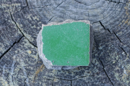 one piece of green small square old ceramic tile lies on a gray wooden table
