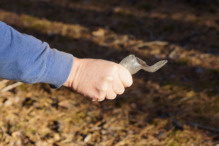 the hand of an aggressive male criminal in blue clothes holds a sharp piece of glass broken bottle on the street on a brown backgroundの写真素材