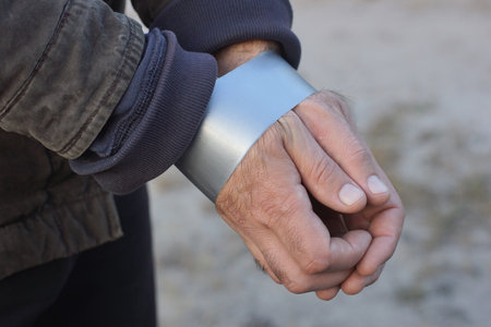 the hands of a male criminal are tied and wrapped with gray tape on a gray background on the street