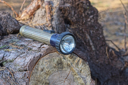 one old gray black metal electric flashlight lies on a pine log on the street in nature