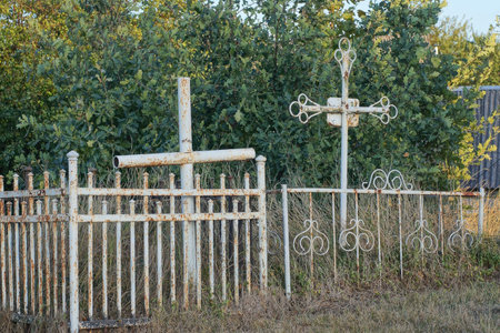 one white metal crosses on a grave behind an iron decorative fence in a cemetery on the streetの写真素材