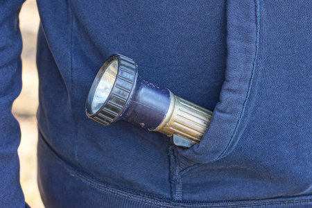 one metal electric black gray flashlight lies in the pocket of a mans winter jacket on the street