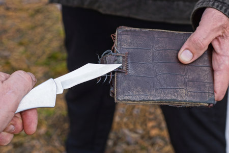 hand of a robber with a gray knife in front of the hand of a man giving away a brown leather wallet on the streetの写真素材
