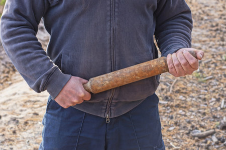 aggressive man in gray blue clothes holding a brown wooden bat in his hands on the street