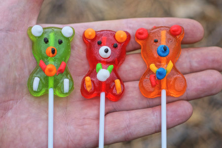 three colored gummies candies in the shape of bears on sticks lie on the palm of the handの写真素材