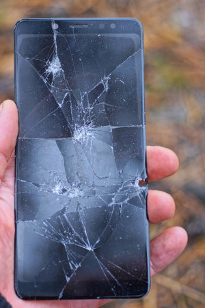 hand holds one broken large smartphone with a black screen in white cracks on the street