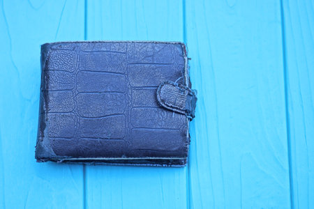 one old closed brown leather wallet lies on a blue wooden tableの写真素材