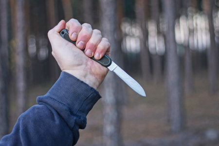 a hand holds one old folding army knife on the street against the background of trees