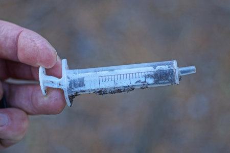 fingers holding one old dirty plastic white syringe on the streetの写真素材