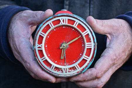 men's hands holding a big old red round alarm clock clock on the streetの写真素材