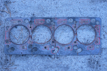 one old black gasket for a car engine lies on the gray sand on the street