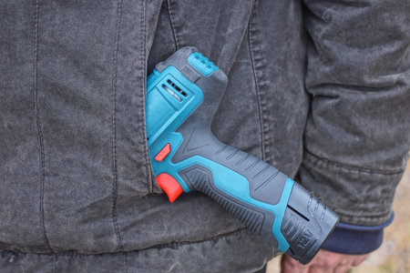 one electric screwdriver lies in the pocket of a gray jacket on a worker on the street