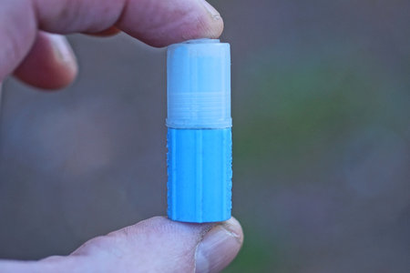 fingers on hand holding a small blue medical plastic tube with a white cap on a gray background
