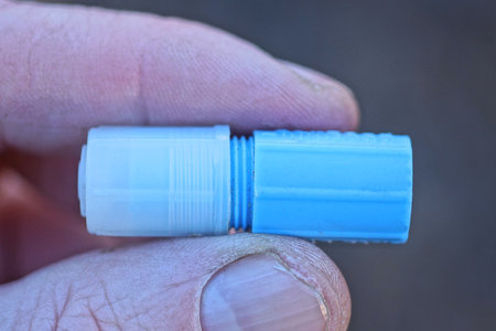 fingers on hand holding a small blue medical plastic tube with a white cap on a gray background