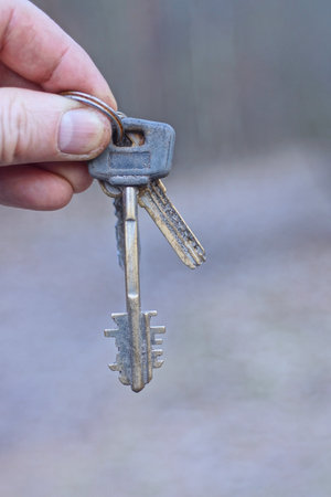a hand holds a bunch of three old metal gray door keys on the street