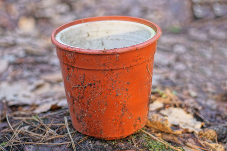 one old dirty red plastic flowerpot pot stands on the gray ground on the street