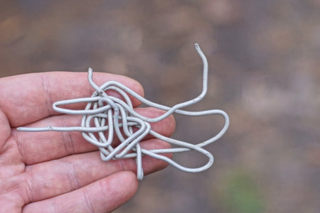 hand holding a piece of old crumpled gray aluminum wire on the street