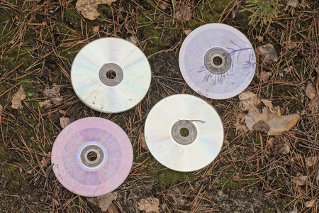 a row of four old dirty compact discs lie on the gray ground on the street